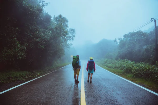 Lover Asian man and Asian women travel nature. Walk on the road route. traveling nature happily. Amid the mist rainy. in the rainy season.