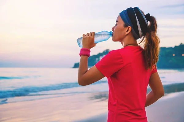 Mulheres asiáticas fazendo exercícios na praia pela manhã. Relaxe com o passeio pelo mar e beba água das garrafas de plástico. praia, esporte, exercício, viajar Tailândia . — Fotografia de Stock