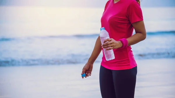 Donne asiatiche che fanno jogging allenamento sulla spiaggia al mattino. Rilassatevi con la passeggiata sul mare e l'acqua potabile dalle bottiglie di plastica. Jogging sulla spiaggia . — Foto Stock