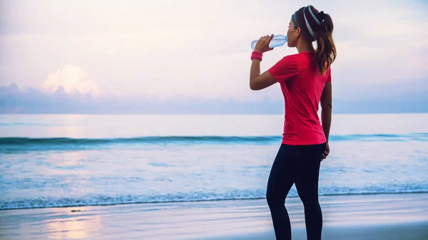 Азіатські жінки бігу тренування на пляжі вранці. Відпочиньте з морською прогулянкою і питною водою з пластикових пляшок. Біг на пляжі — стокове фото