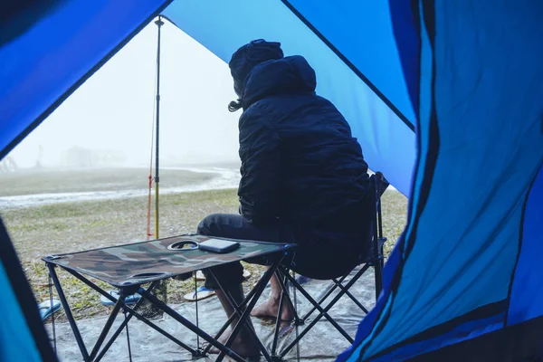 Asian man travel relax in the holiday. camping on the Mountain. sit relax on the chair. In the atmosphere rain fall have fog down. countryside, Forest, route, summer, nature, outdoor, holiday, relax, travel Thailand, landscape, style.