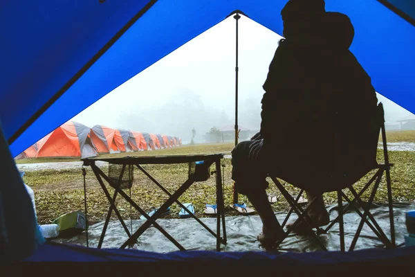 Asian man travel relax in the holiday. camping on the Mountain. sit relax on the chair. In the atmosphere rain fall have fog down. camping, countryside, Forest, tent,  nature, outdoor, holiday, relax, travel, summer, travel Thailand.