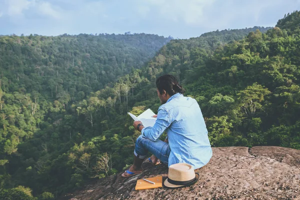 Viagem homem asiático relaxar no feriado. assentos relaxar ler livros em penhascos rochosos. Na Montanha. Na Tailândia — Fotografia de Stock