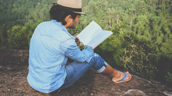 Asiatische Männer reisen entspannt in den Urlaub. Sitzgelegenheiten entspannen lesen Bücher auf felsigen Klippen. auf dem Berg. in Thailand — Stockfoto