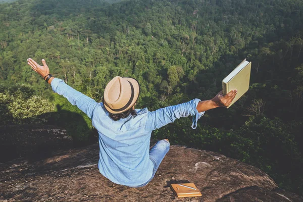 Viagem homem asiático relaxar no feriado. assentos relaxar ler livros em penhascos rochosos. Na Montanha. Na Tailândia — Fotografia de Stock