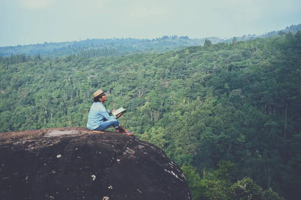 Viagem homem asiático relaxar no feriado. assentos relaxar ler livros em penhascos rochosos. Na Montanha. Na Tailândia — Fotografia de Stock