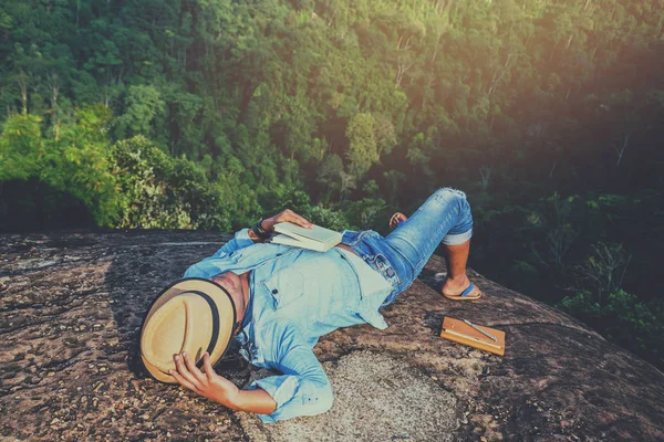 Hombre asiático viajar relajarse en las vacaciones. dormir relajarse leer libros sobre acantilados rocosos. En la montaña. En Tailandia — Foto de Stock
