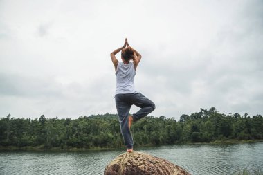 Asian women relax in the holiday. Play if yoga. On the rocks in the middle of the water clipart