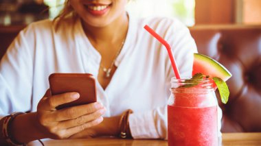 Asyalı kadın arkanıza yamave meyve içmek dinlenmek. Ve telefon tutuyor..