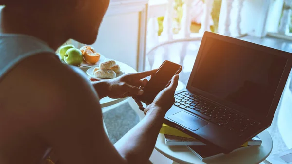 Man is working sitting on the sofa. Hands are holding mobile phone and  working with a notebook