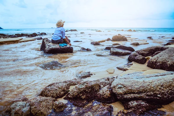 Ασιατικές γυναίκα ταξιδεύουν φύση. Τα ταξίδια χαλαρώνουν. κάθονται και χαλαρώνουν στα βράχια στη θάλασσα του Πουκέτ. στην Ταϊλάνδη. Καλοκαίρι. — Φωτογραφία Αρχείου