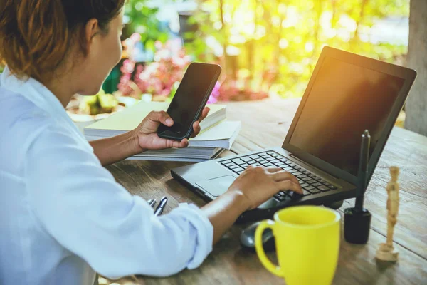 Masada oturan Asyalı kadın. tatilde çalışan dizüstü bilgisayar, akıllı telefon ve kahve fincan. Bilgisayar ekranında.