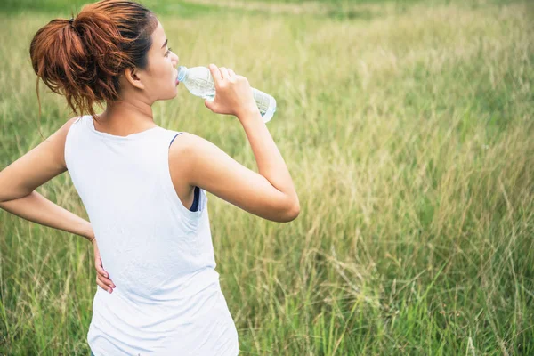 As mulheres asiáticas relaxam nas férias. Beba a água em um pasto verde — Fotografia de Stock