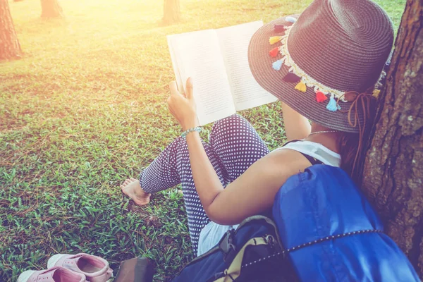 Las mujeres asiáticas viajan relajarse en las vacaciones. Lea el libro debajo del árbol en el prado en el parque . — Foto de Stock