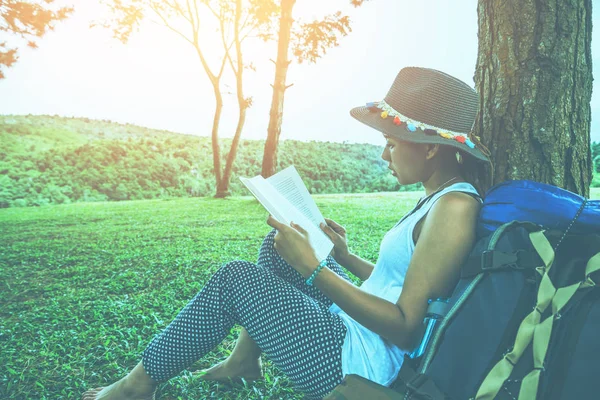 아시아 여성들은 휴일에 편안 한 여행을 한다. 공원의 초원에 있는 나무 아래서 책을 읽는다. — 스톡 사진