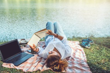 Women sitting a relax working with a notebook and lying reading a book during a relax in the park. in the holiday. summer clipart
