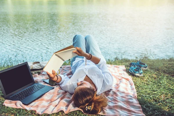 Les femmes assis un relax travailler avec un cahier et couché lire un livre pendant une détente dans le parc. pendant les vacances. été — Photo