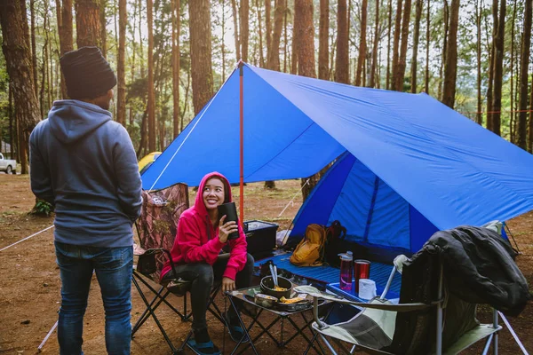 Jovem casal asiático de feliz apreciando Acampar na floresta de pinheiros Sente-se e coma comida na página Camping no meio da natureza . — Fotografia de Stock