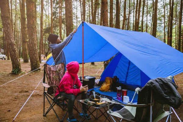 Jovem casal asiático de feliz apreciando Acampar na floresta de pinheiros Sente-se e coma comida na página Camping no meio da natureza . — Fotografia de Stock