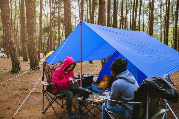 Jong Aziatisch paar gelukkig genieten Kamperen in het dennenbos Zit en eet eten op de Camping pagina in het midden van de natuur. — Stockfoto