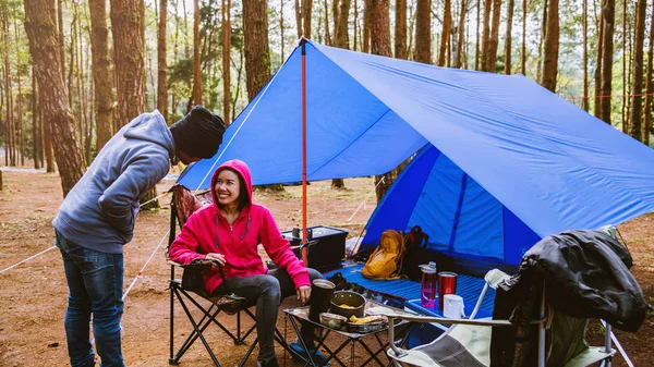 Jovem casal asiático de feliz apreciando Acampar na floresta de pinheiros Sente-se e coma comida na página Camping no meio da natureza . — Fotografia de Stock