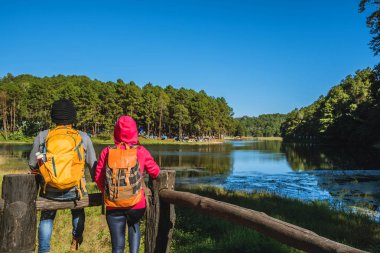 Sırt çantalı bir çift gezgin güzel bir bakış açısıyla, sisli göl yüzeyinde güneşin doğuşunun tadını çıkarıyorlar genç erkekler ve Asyalı sevgililer Tayland 'daki Pang Ung parkında doğayı geziyorlar..