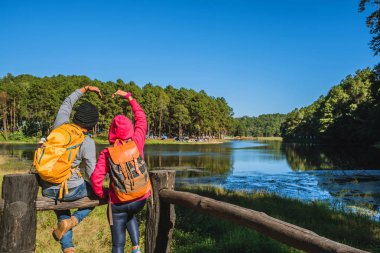 Sırt çantalı bir çift gezgin güzel bir bakış açısıyla, sisli göl yüzeyinde güneşin doğuşunun tadını çıkarıyorlar genç erkekler ve Asyalı sevgililer Tayland 'daki Pang Ung parkında doğayı geziyorlar..