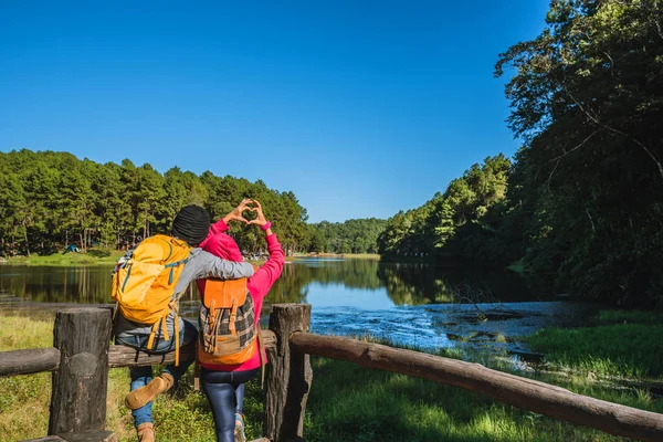 Párové cestovatele s batohem rádi relaxovat na horách, s jezery, krásné rybníky borovicové lesy. páry zvednou ruce, aby vytvořily tvar srdce. Šťastná a sladká láska. — Stock fotografie