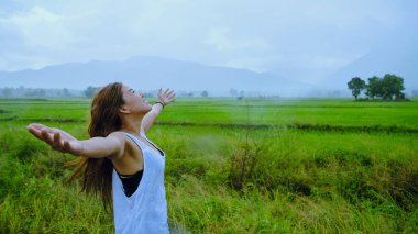 Asyalı kadınlar tatillerde rahatça seyahat eder. Kız mutlu bir şekilde gülümsedi ve yağan yağmurun tadını çıkardı. Ülkelerde seyahat, yeşil pirinç tarlaları, Tayland seyahatleri..