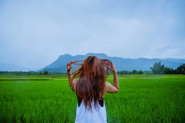 Asiatische Frauen reisen entspannt in den Urlaub. Das Mädchen lächelte glücklich und genoss den Regen, der fiel. Reisen auf dem Land, grüne Reisfelder, Reisen nach Thailand. — Stockfoto