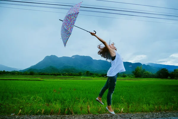 Asiatische Frauen reisen entspannt in den Urlaub. Die Frauen standen glücklich mit einem Regenschirm im Regen und genossen den Regen, der fällt. Reisen in ländliche Gegenden, grüne Reisfelder, Reisen nach Thailand. — Stockfoto