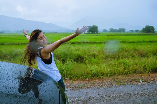 Asijské ženy cestují odpočívat v dovolené.Dívka se šťastně usmála a užila si padající déšť. Turistická jízda po venkově během období dešťů, Zelená rýžová pole, Cestovní Thajsko. — Stock fotografie