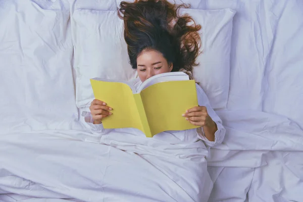 Молодая женщина спит в постели. Вид сверху на спящую в кровати молодую женщину. Расслабься, юная улыбающаяся красавица лежит в постели. Спите, читайте книгу на кровати. образование, чтение . — стоковое фото