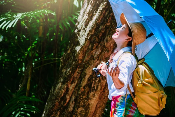 Junges Mädchen mit Rucksack genießt das Reisen Natur im Wald sattgrüne Bäume. glücklich lächelnde Frau mit Naturreisen, ländlichem Wald. im Sommer, Reisen entspannen, Reisen nach Thailand. — Stockfoto