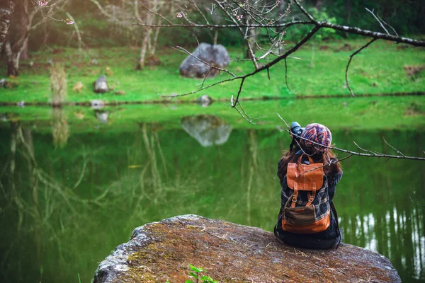 Jonge vrouwen reizen in de winter naar de natuur. Ze zat op de rotsen aan het water in het park. in de zomer — Stockfoto