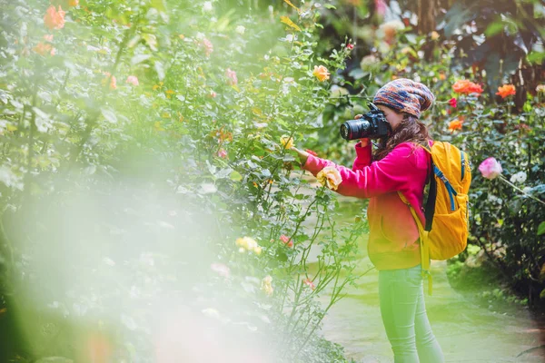Dívka stojící s fotoaparátem a fotografování růží v zahradě. — Stock fotografie