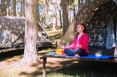 Young Asian woman doing yoga while camping in the forest clipart