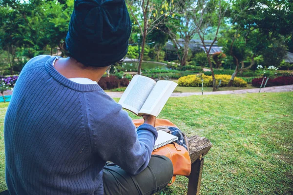 तो तरुण उद्यानात पुस्तक वाचत होता. नैसर्गिक झाडे आणि सुंदर फुलांच्या बागेत — स्टॉक फोटो, इमेज