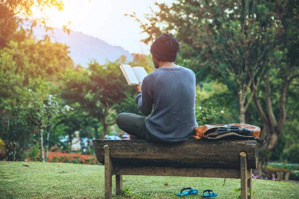 El joven viaja por la naturaleza en la montaña, está sentado y relajado, leyendo un libro en el jardín de flores . — Foto de Stock