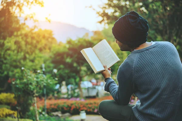 Der junge mann reist in die natur auf den berg, sitzt und relaxt, liest ein buch im blumengarten. — Stockfoto