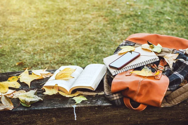 De rugzak en het boek rust op een antieke houten tafel, notitieboekjes, telefoons en de aard van esdoornbladeren van bovenaf. — Stockfoto