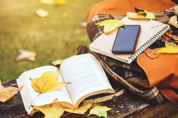 De rugzak is geplaatst op een antieke houten tafel met boeken, notitieboekjes, telefoons en de aard van esdoornbladeren van bovenaf. — Stockfoto