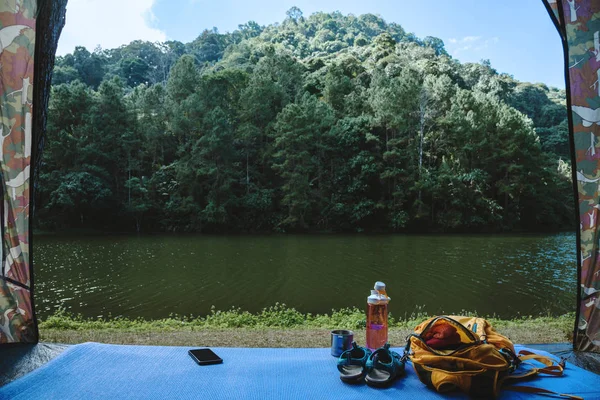 Reisenatur. Reisen entspannen. Rucksack und Schuhe Handy mit einem traveler.sun set vor dem Zelt camping platziert. Hintergrund der Bergsee-Natur. — Stockfoto