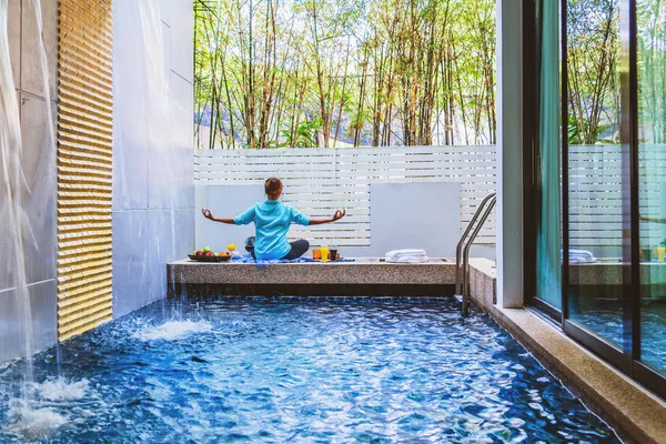 Dívka dělá jógu fitness cvičení pro relaxaci a meditaci u bazénu Uvnitř v domě, během meditace s pomerančovým džusem a ovocem, jablka, pomeranče umístěné na boku. — Stock fotografie