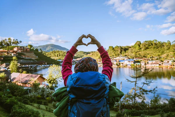 Een meisje met een rugzak die geniet van het reizen op een berg op het platteland. Meisje blij met ontspannen toerisme, stak ze haar hand op om een hartvorm te maken. — Stockfoto