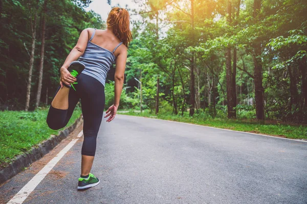 Le donne si allenano per strada. Parco naturale. Ragazza che sta sollevando le gambe per esercitare. esercizio, corsa . — Foto Stock