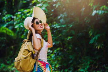 Sırt çantalı genç kız ormandaki yemyeşil ağaçların tadını çıkarıyor. Mutlu, gülen bir kadın doğa yolculuğu, kırsal kesimde orman. Yazın seyahat, dinlenme, Tayland seyahati..