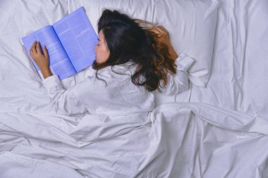 Yatakta Uyuyan Genç Kadın. Yatakta rahat uyuyan genç bir kadın manzarası. Yatakta kitap okuyan ve uyuyan kız. uyku, rahatlama, uyku, eğitim, okuma; kitap, keyif, mutluluk, derin uyku.