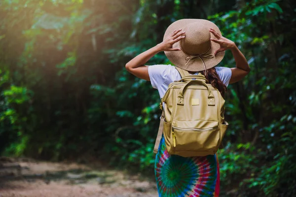 푸른 나무들이 우거진 숲 속을 자연 속을 여행하는 여행 가방을 든 소녀. 숲 속을 걷고 있는 소녀의 뒷모습. 여름에는 휴식을 취하고, 태국을 여행하고,. — 스톡 사진
