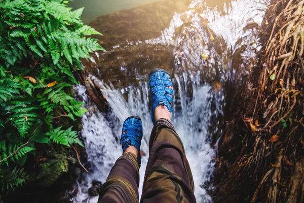 Azjatka podróżuje naturą. Podróżuj spokojnie. Widok z góry na nogi dziewczyny w niebieskich butach. Podnosi nogi unosząc się na wodospadzie. natura, tło, lato, wakacje, turystyka. — Zdjęcie stockowe